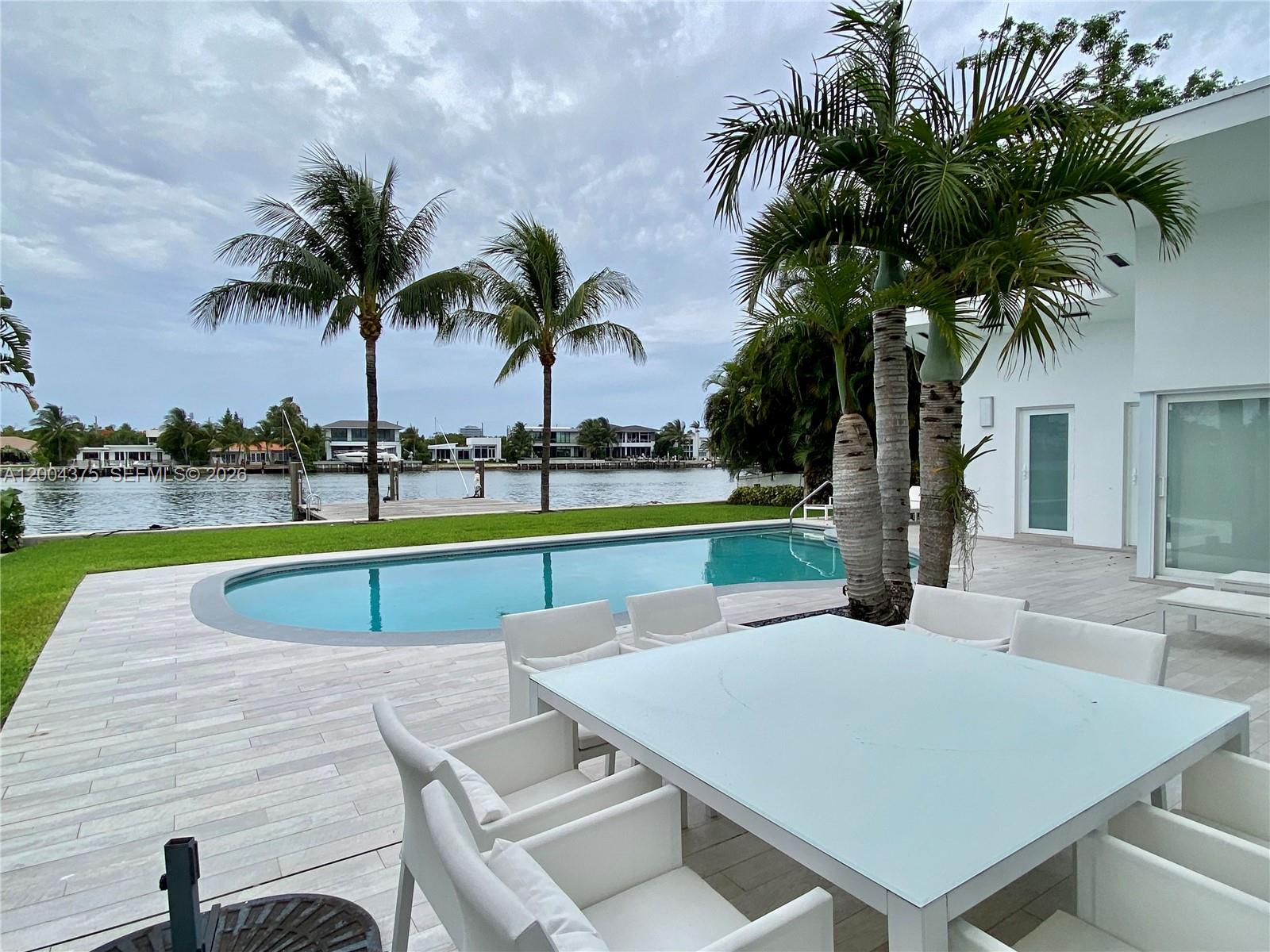 A patio with a dining set and swimming pool overlooks a canal with palm trees — 265 N Shore Dr, Miami Beach FL 33141, MIAMI BEACH, FL