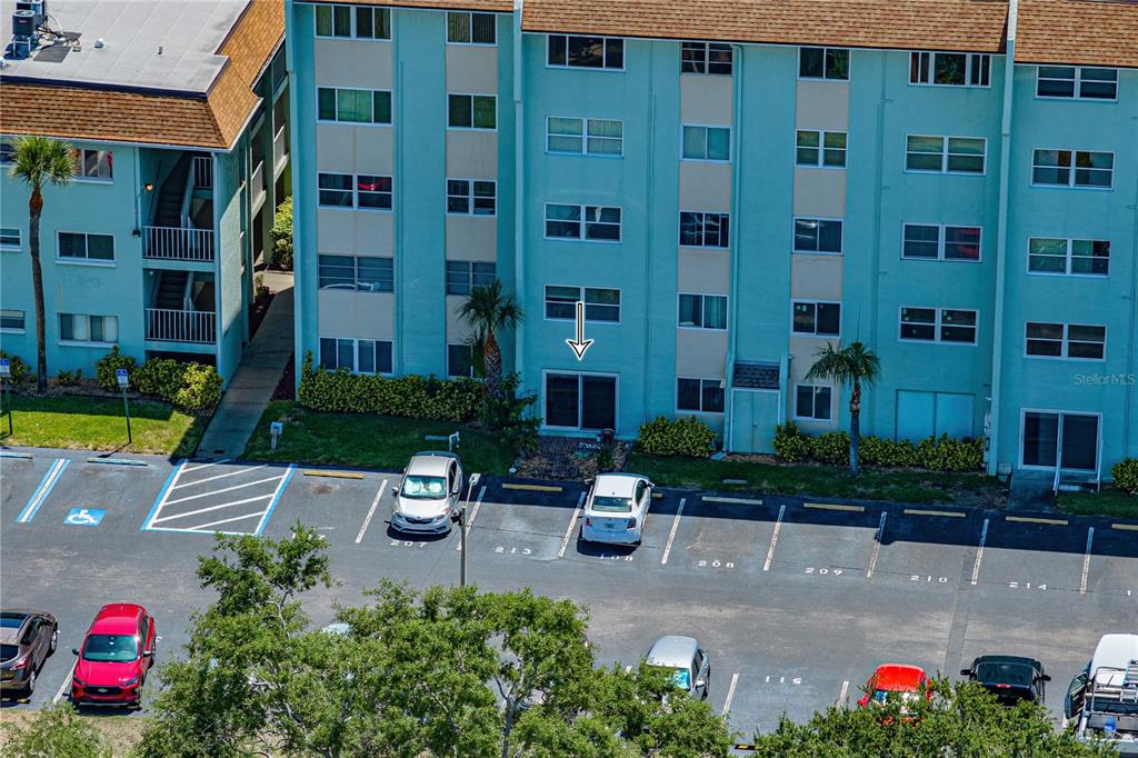 An exterior view of a multi-story teal apartment building with a parking lot in front — 801 83RD AVENUE N UNIT 108, ST PETERSBURG, FL
