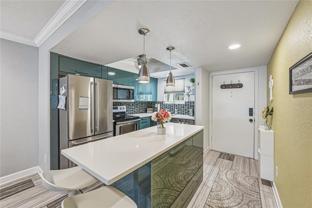 A modern kitchen features teal cabinets, stainless steel appliances, and a white quartz island — 801 83RD AVENUE N UNIT 108, ST PETERSBURG, FL
