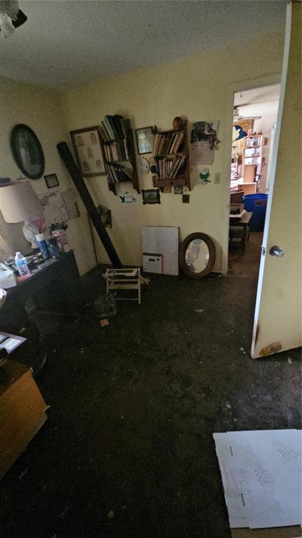 A cluttered room with yellow walls, wall-mounted bookshelves, and a doorway leading to another area — 2116 WINNETKA COURT, ORLANDO, FL