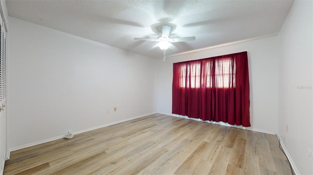 An empty bedroom features light wood-look flooring, white walls, and red curtains over a window — 4460 IRONWOOD CIRCLE UNIT 407A, BRADENTON, FL