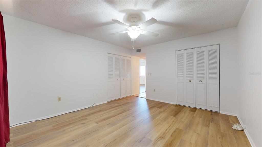 A bedroom with white walls, light wood-look flooring, a ceiling fan, and two louvered closets — 4460 IRONWOOD CIRCLE UNIT 407A, BRADENTON, FL