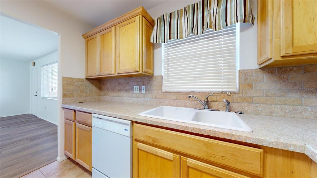 A kitchen features light wood cabinets, a white dishwasher, a double sink, and tiled backsplash — 4460 IRONWOOD CIRCLE UNIT 407A, BRADENTON, FL