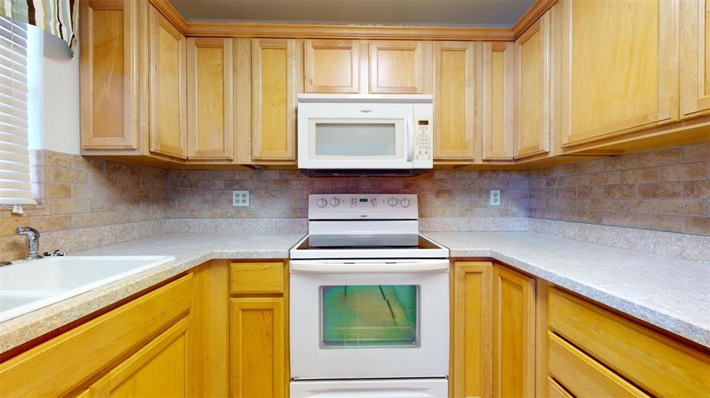 A kitchen features light wood cabinets, white appliances, and a tan brick-style backsplash — 4460 IRONWOOD CIRCLE UNIT 407A, BRADENTON, FL