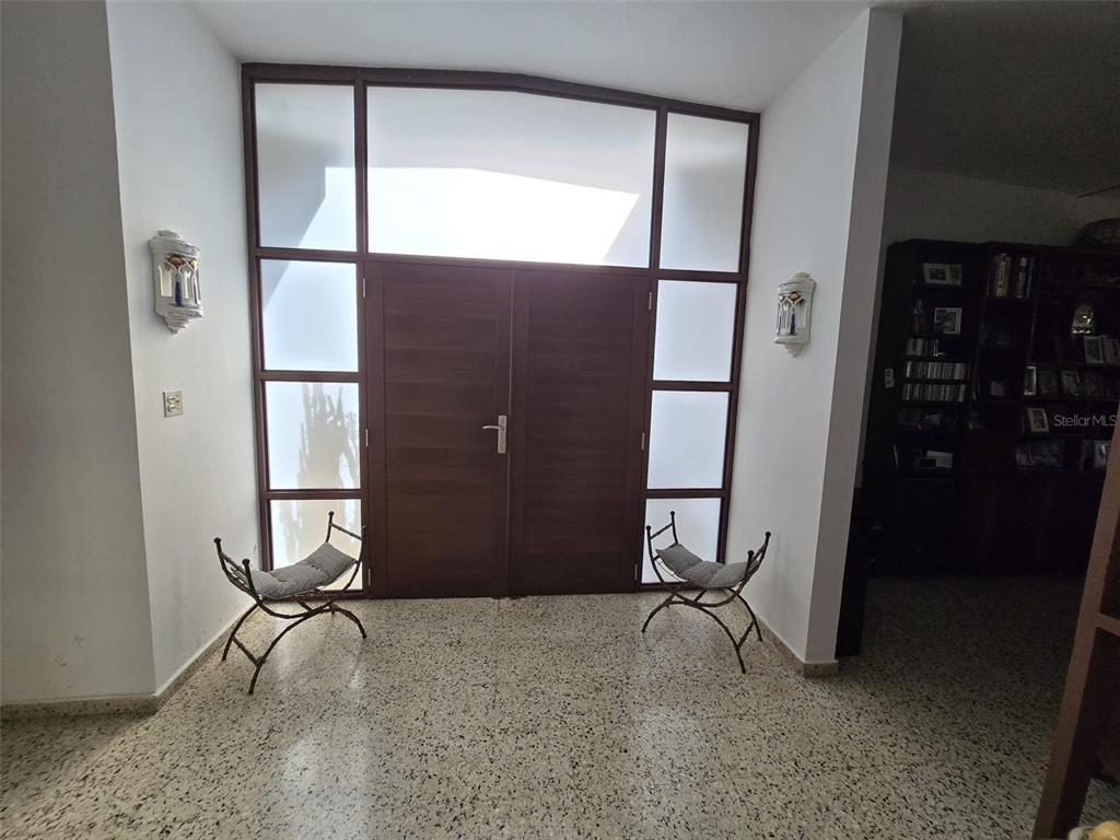An entryway features double wooden doors, frosted glass panels, and two metal chairs on terrazzo flooring — 68 SOCORRO STREET, QUEBRADILLAS, PR
