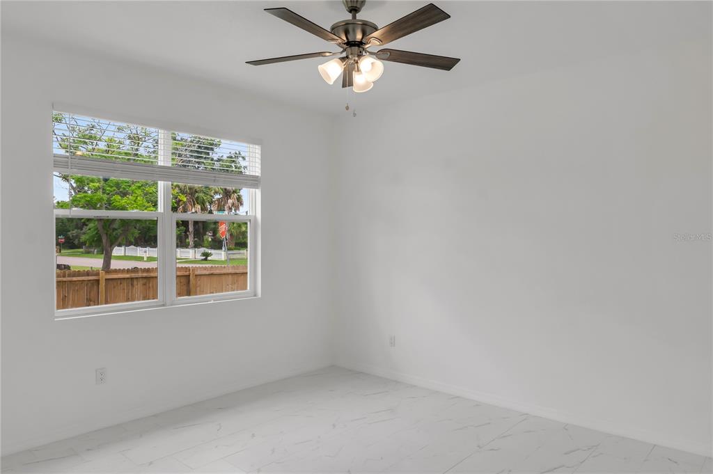 A bright, empty room features white walls, marble-look tile flooring, and a ceiling fan — 4733 ABACA STREET, ORLANDO, FL