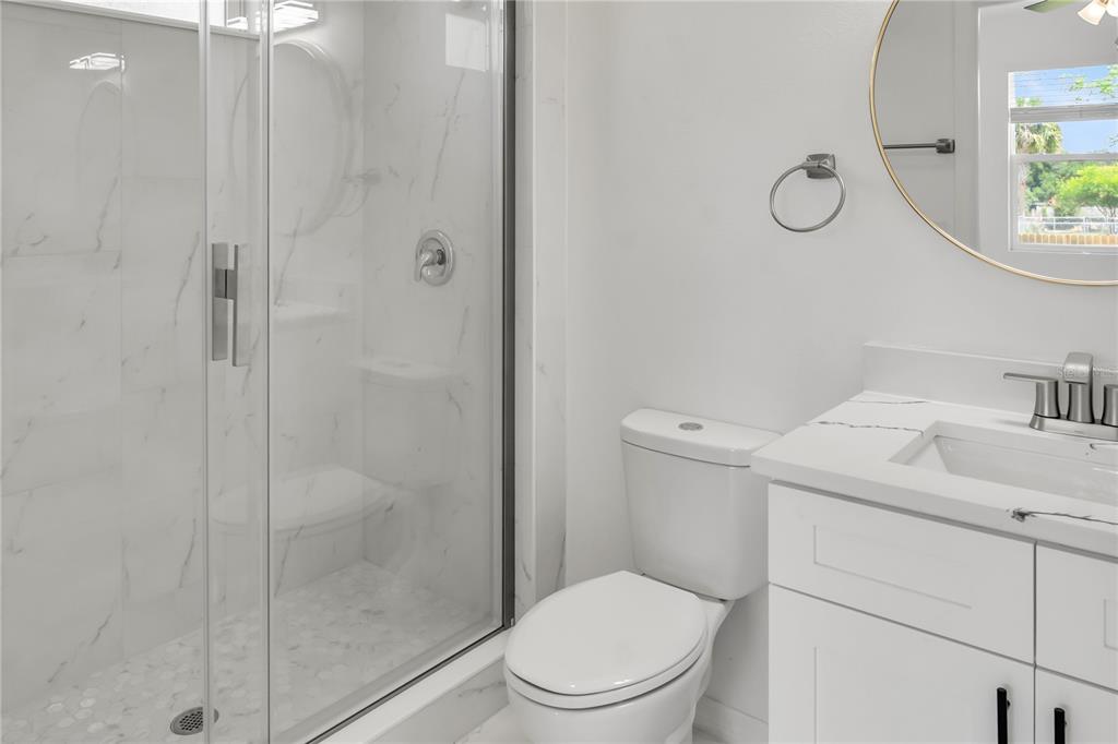 A modern bathroom features a glass-enclosed shower, a white vanity, and a round wall mirror — 4733 ABACA STREET, ORLANDO, FL