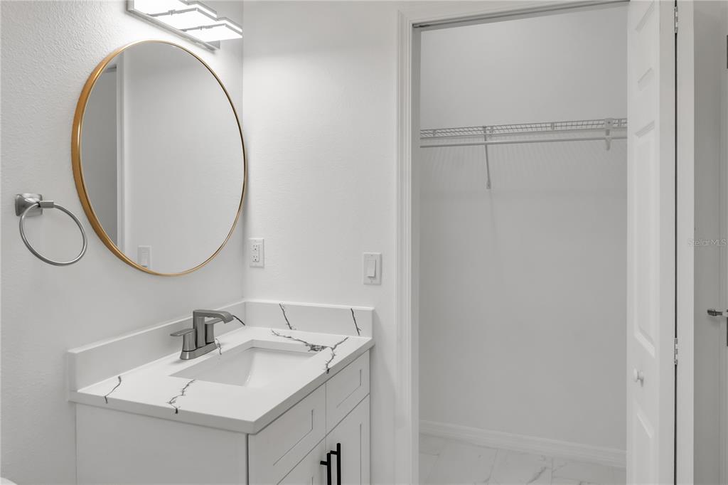 A bathroom vanity with a marble countertop, round mirror, and an adjacent walk-in closet — 4733 ABACA STREET, ORLANDO, FL