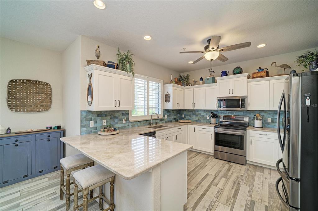 A kitchen features white cabinets, a stone island, blue tile backsplash, and wood-look flooring — 3607 10TH LANE W, PALMETTO, FL