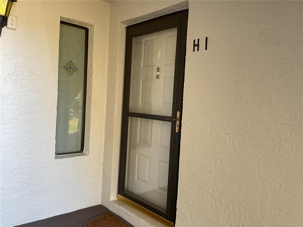 A front entrance features a brown storm door, a side window, and the unit number H1 — 2687 PINE RIDGE WAY S UNIT H1, PALM HARBOR, FL