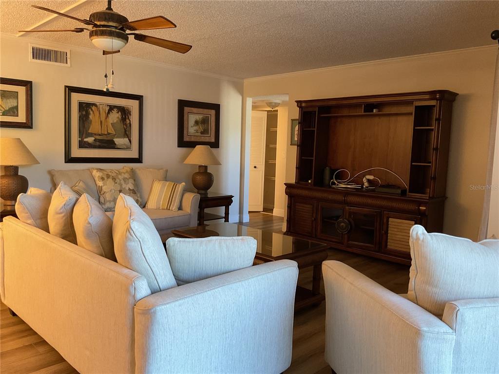 A living room features light-colored sofas, a large wooden entertainment center, and a ceiling fan — 2687 PINE RIDGE WAY S UNIT H1, PALM HARBOR, FL