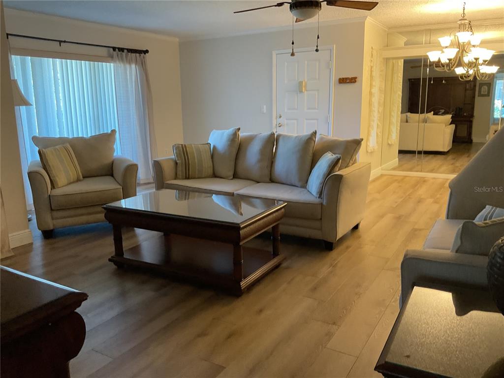 A living room features light-colored furniture, a dark wood coffee table, and wood-look flooring — 2687 PINE RIDGE WAY S UNIT H1, PALM HARBOR, FL