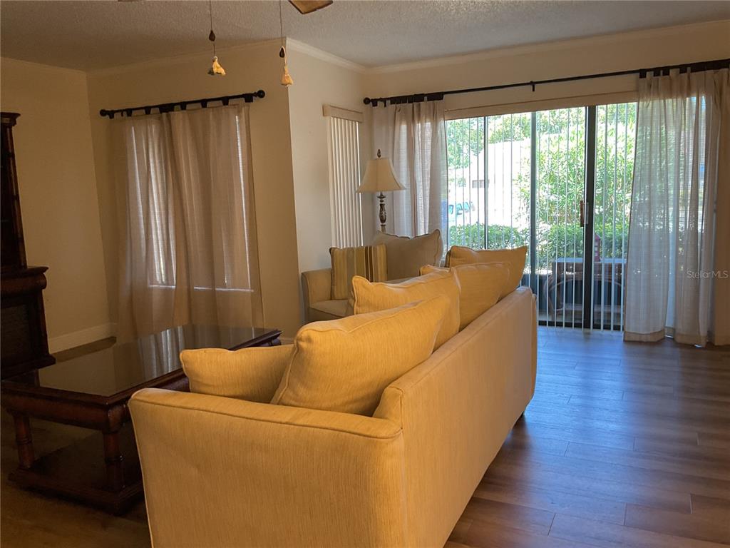 A living room features a tan sofa, wood-look flooring, and sliding glass doors to a patio — 2687 PINE RIDGE WAY S UNIT H1, PALM HARBOR, FL
