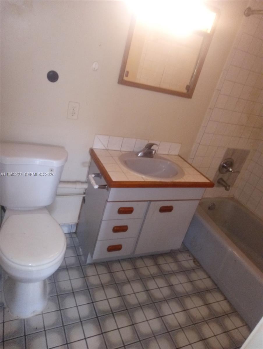 A bathroom features a white toilet, a vanity with a tiled countertop, and a bathtub — 1925 Harding St # D, Hollywood FL 33020, HOLLYWOOD, FL