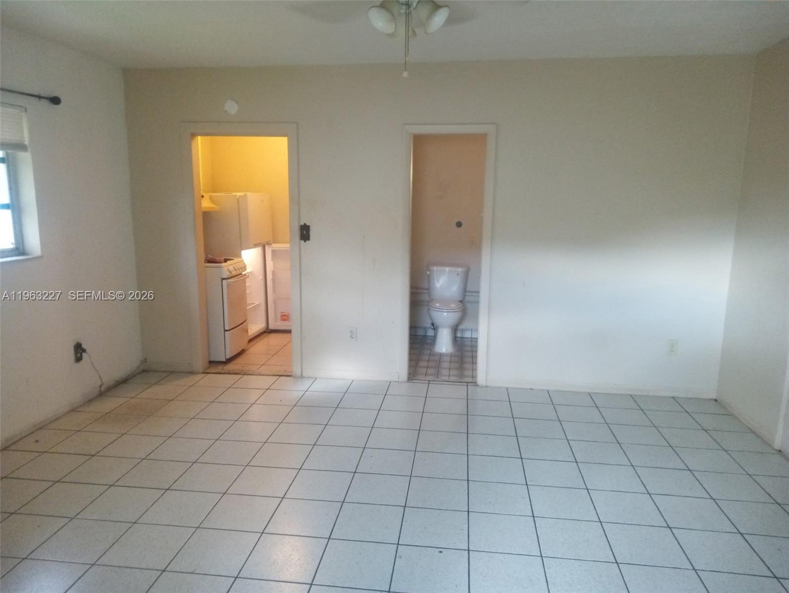 An interior room with white tile flooring features doorways leading to a kitchen and bathroom — 1925 Harding St # D, Hollywood FL 33020, HOLLYWOOD, FL