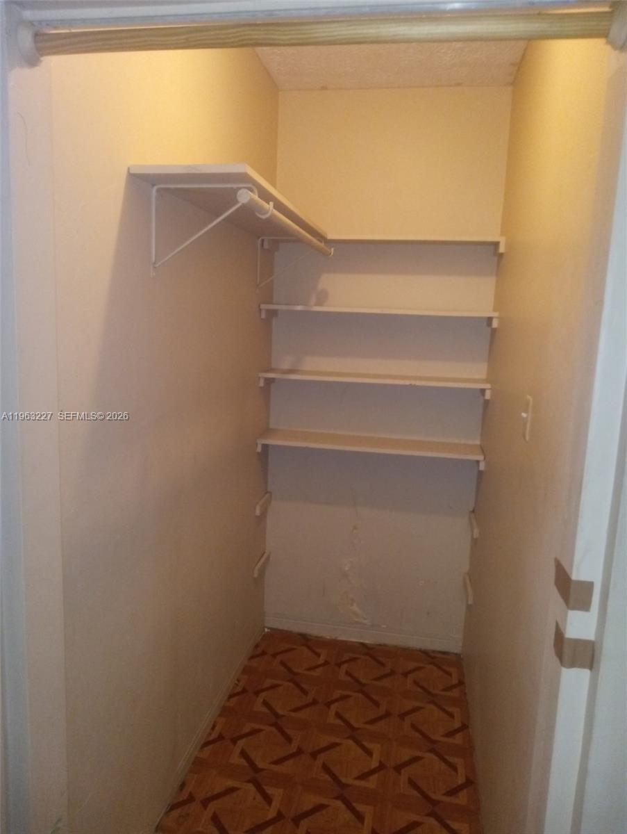 A small closet features white shelving, a wooden hanging rod, and patterned tile flooring — 1925 Harding St # D, Hollywood FL 33020, HOLLYWOOD, FL