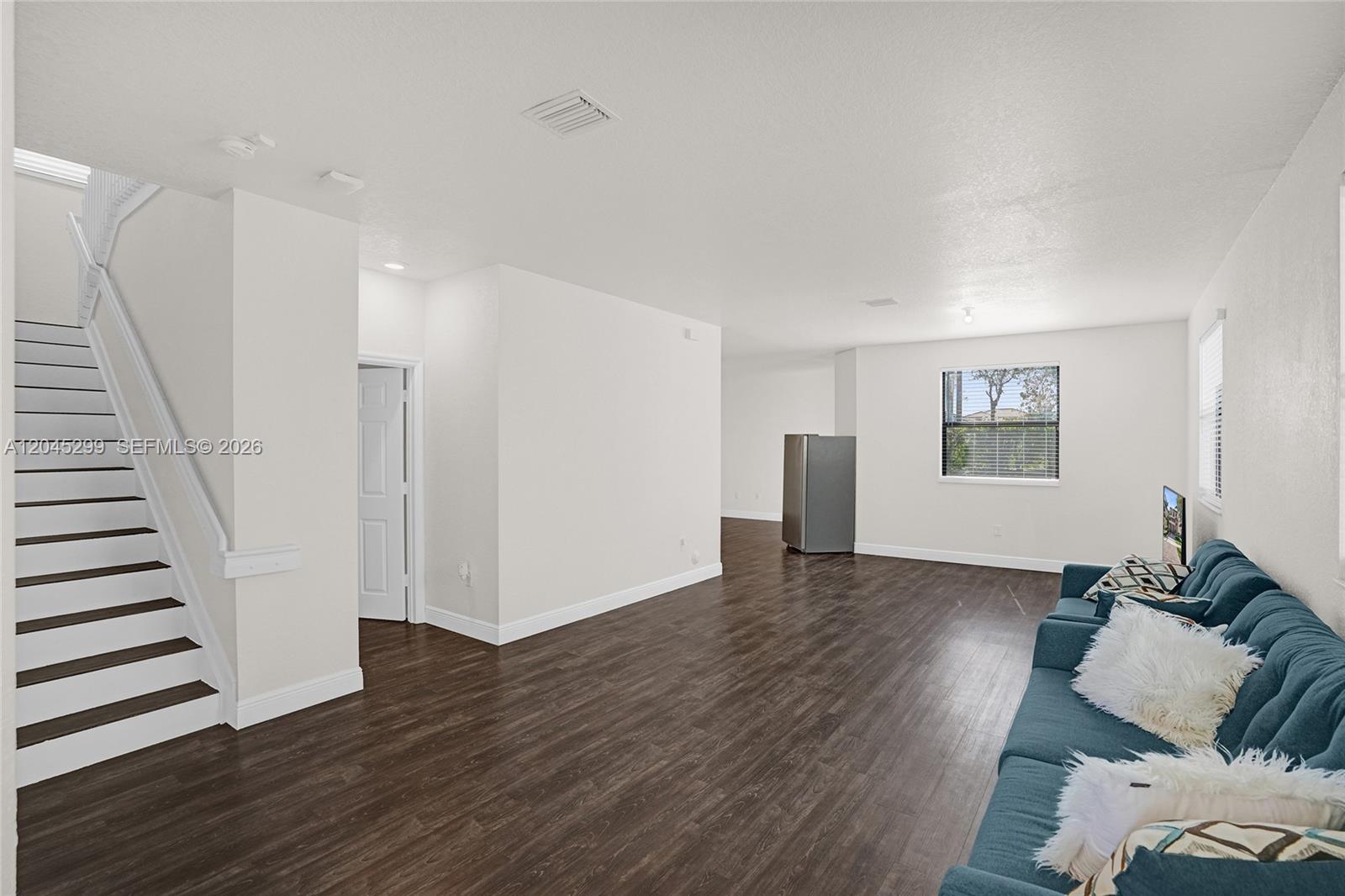 A living room features dark wood-look flooring, a staircase, and a blue sofa — 2502 NE 1st St # 0, Homestead FL 33033, HOMESTEAD, FL