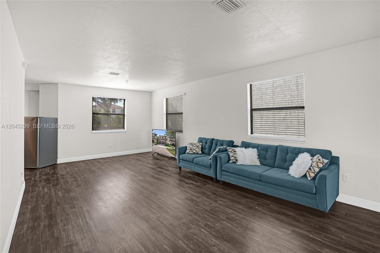 A living room features dark wood-look flooring, white walls, two blue sofas, and two windows — 2502 NE 1st St # 0, Homestead FL 33033, HOMESTEAD, FL