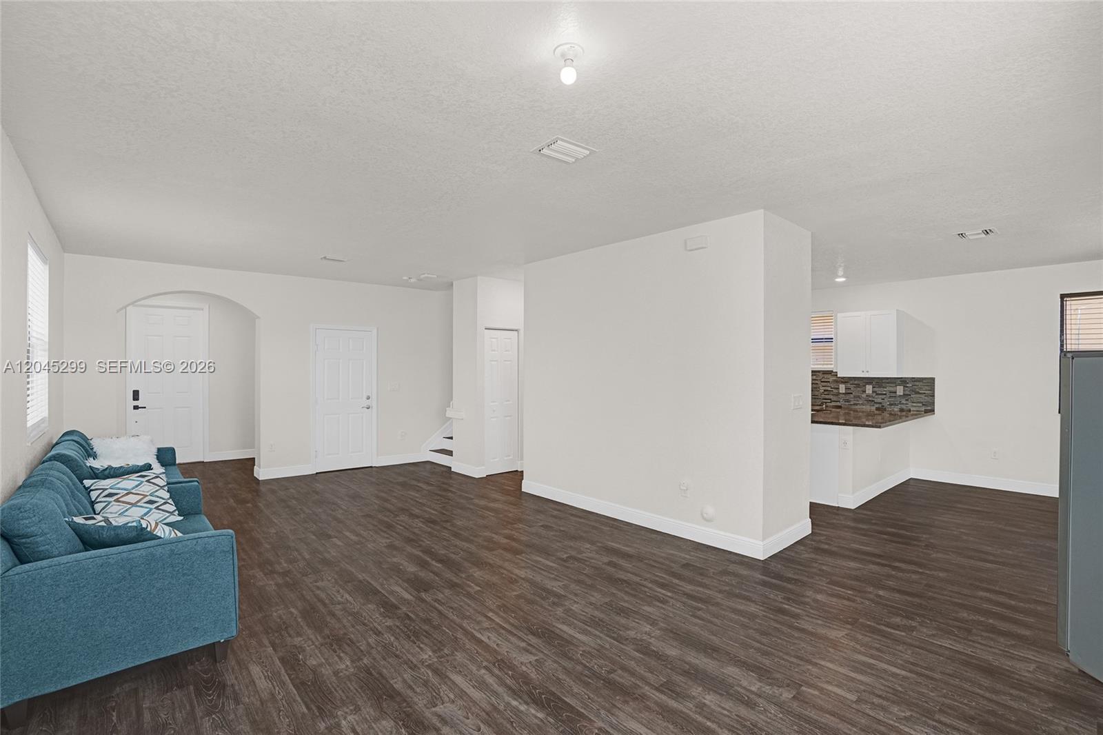 A living room with dark wood-look flooring connects to an open kitchen with white cabinets — 2502 NE 1st St # 0, Homestead FL 33033, HOMESTEAD, FL