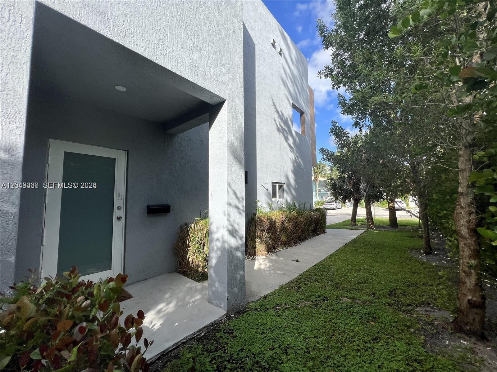 A modern gray house features a recessed entryway, a concrete walkway, and surrounding green landscaping — 1121 NE 23rd Ter # 1121, Pompano Beach FL 33062, POMPANO BEACH, FL