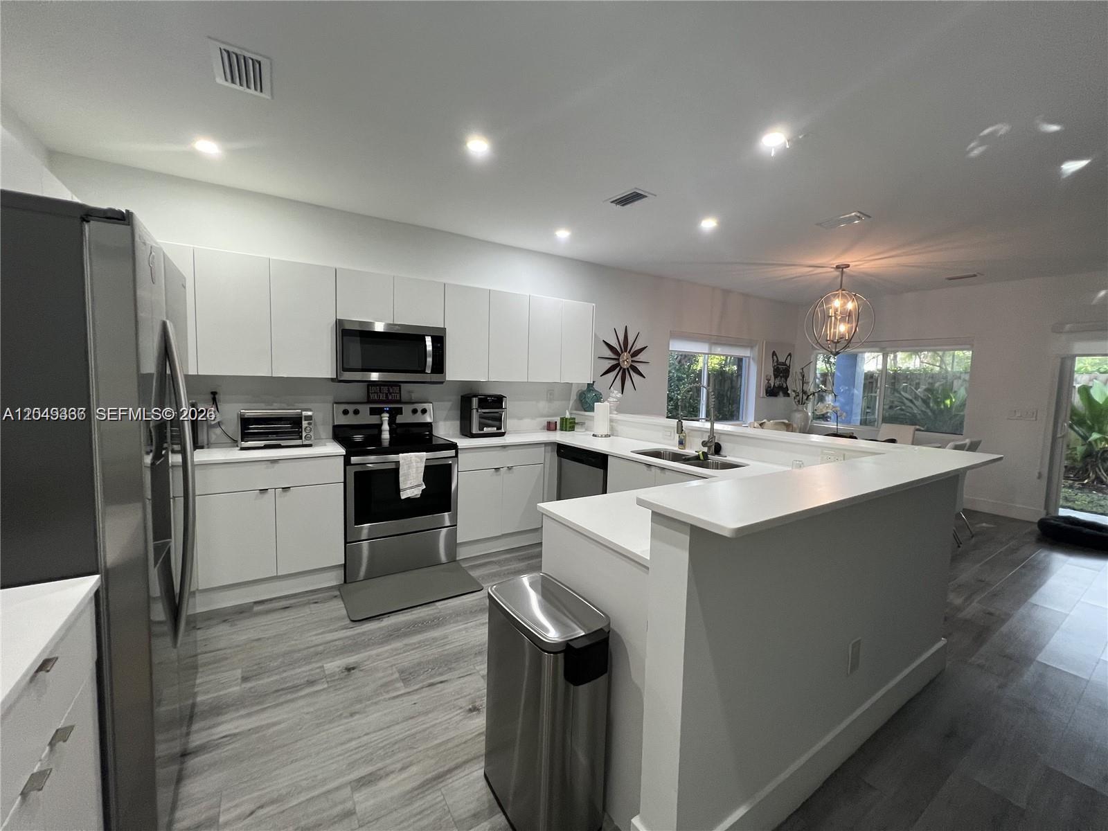 A modern kitchen features white cabinetry, stainless steel appliances, and light-colored wood-look flooring — 1121 NE 23rd Ter # 1121, Pompano Beach FL 33062, POMPANO BEACH, FL