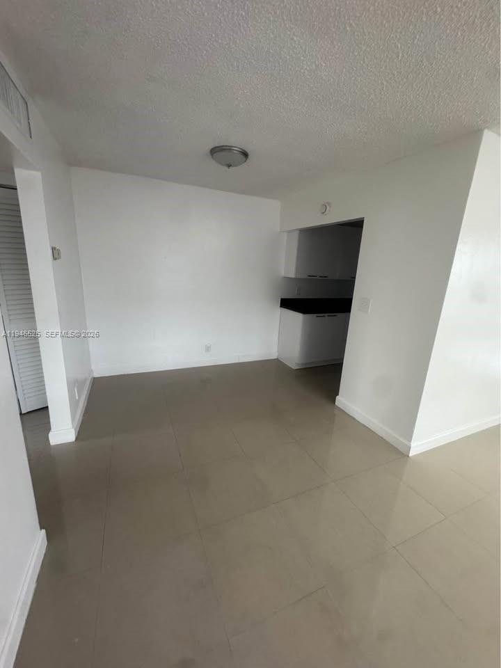An empty room with light-colored tile flooring leads into a small kitchen area — 2019 Jackson St # 105, Hollywood FL 33020, HOLLYWOOD, FL