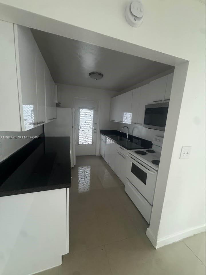 A galley-style kitchen features white cabinets, black countertops, and white appliances — 2019 Jackson St # 105, Hollywood FL 33020, HOLLYWOOD, FL