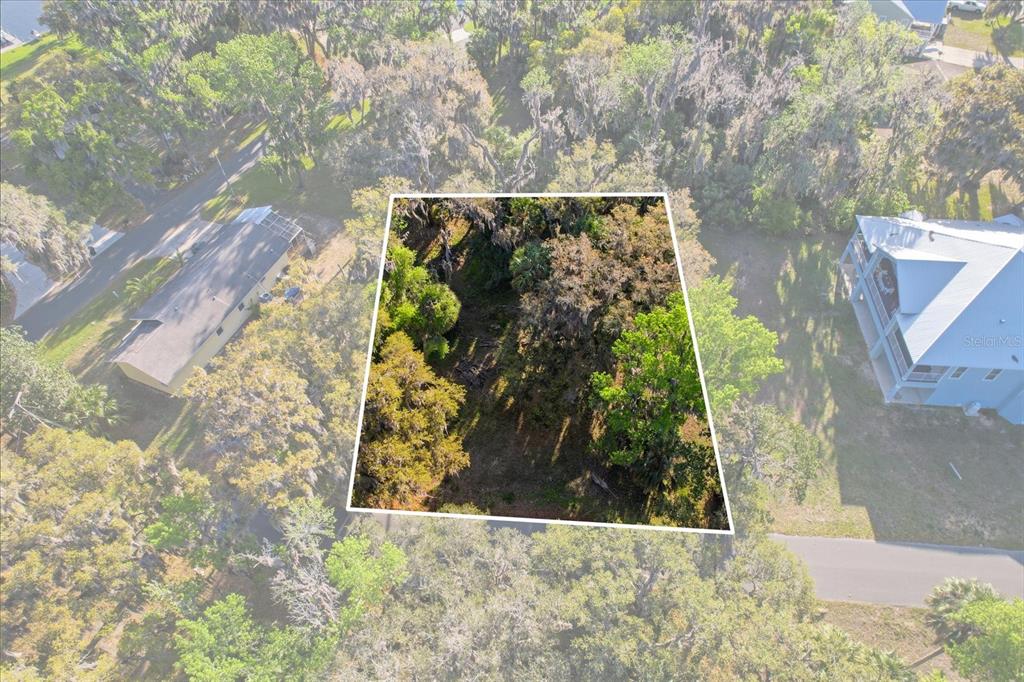 An aerial view shows a wooded, rectangular vacant lot situated between two residential properties — 20 NW MAGNOLIA CIRCLE, CRYSTAL RIVER, FL