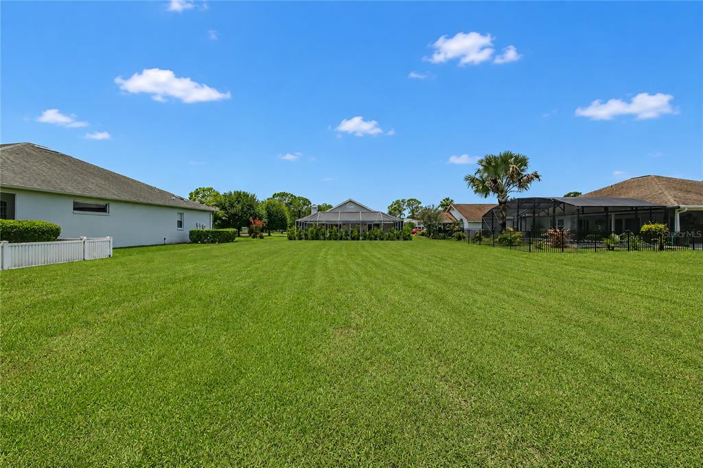 A large, grassy backyard sits between two houses under a bright blue sky — 2013 BEAVER CREEK DRIVE, PORT ORANGE, FL