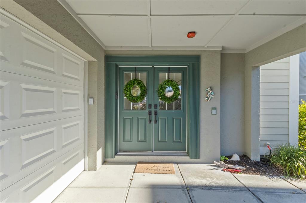 A teal double front door with wreaths sits under a covered entryway beside a garage — 515 FOREST WAY, LONGBOAT KEY, FL