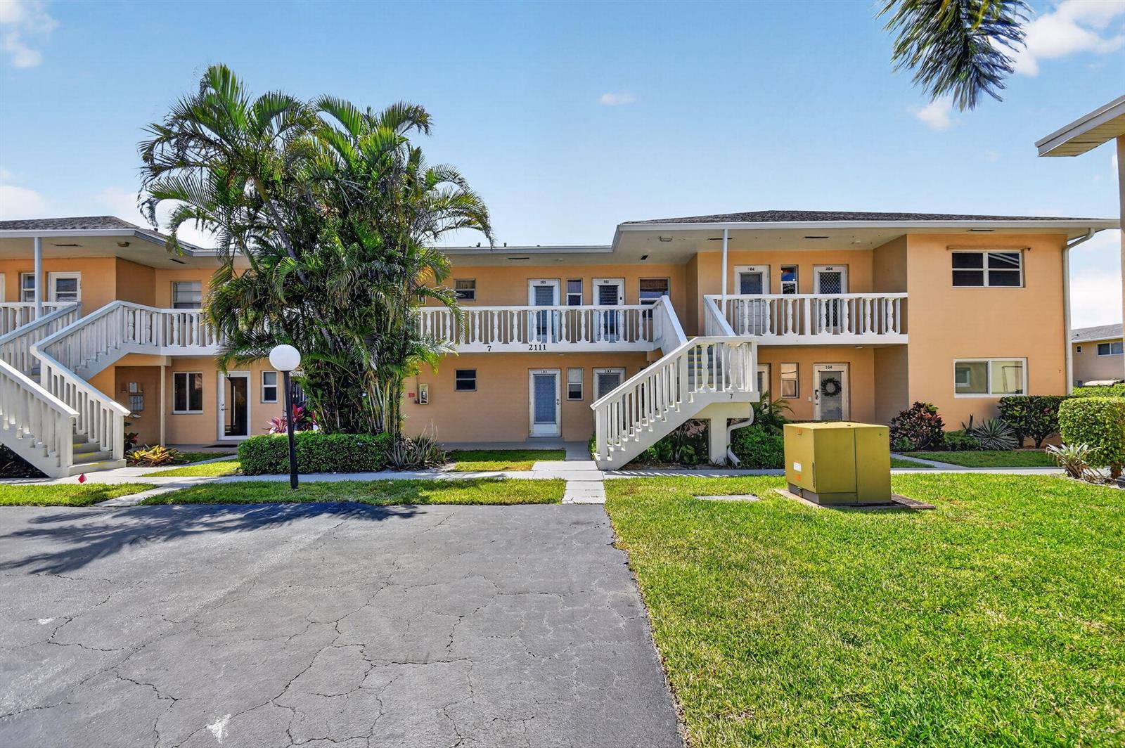 A two-story apartment building with tan stucco walls, white railings, and an outdoor staircase — 2111 NE 1st Court # 204, Boynton Beach FL 33435, BOYNTON BEACH, FL