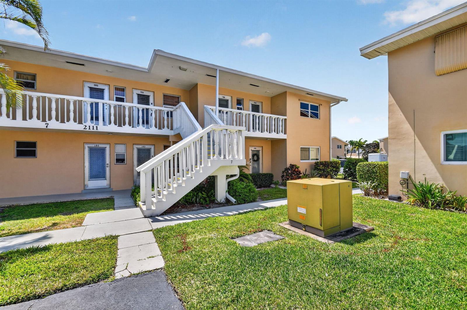 A two-story apartment building with yellow stucco walls, white railings, and an exterior staircase — 2111 NE 1st Court # 204, Boynton Beach FL 33435, BOYNTON BEACH, FL