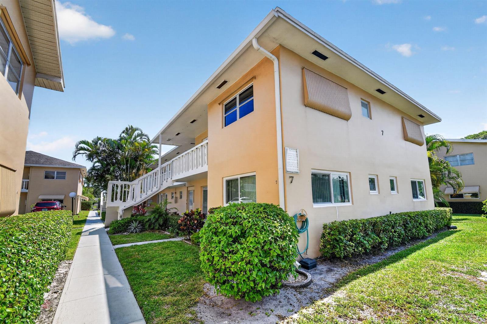 A two-story apartment building with a beige exterior, white railings, and a landscaped lawn — 2111 NE 1st Court # 204, Boynton Beach FL 33435, BOYNTON BEACH, FL