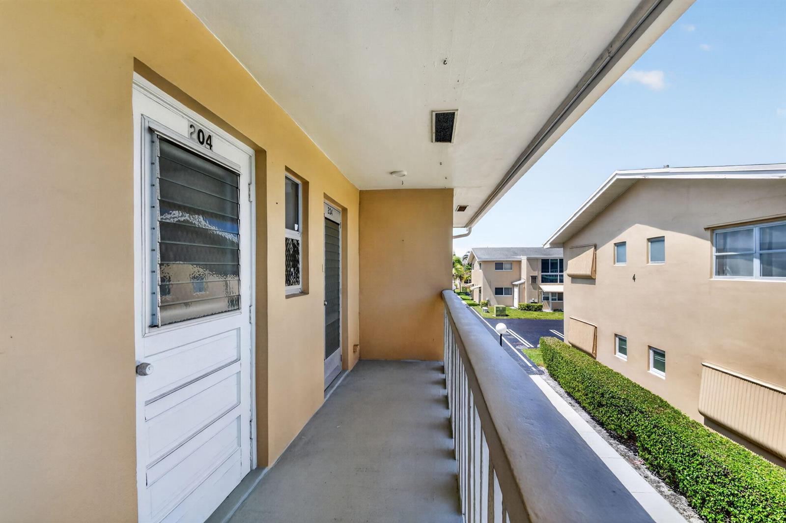 An outdoor walkway with two apartment doors leads to a balcony overlooking a complex — 2111 NE 1st Court # 204, Boynton Beach FL 33435, BOYNTON BEACH, FL