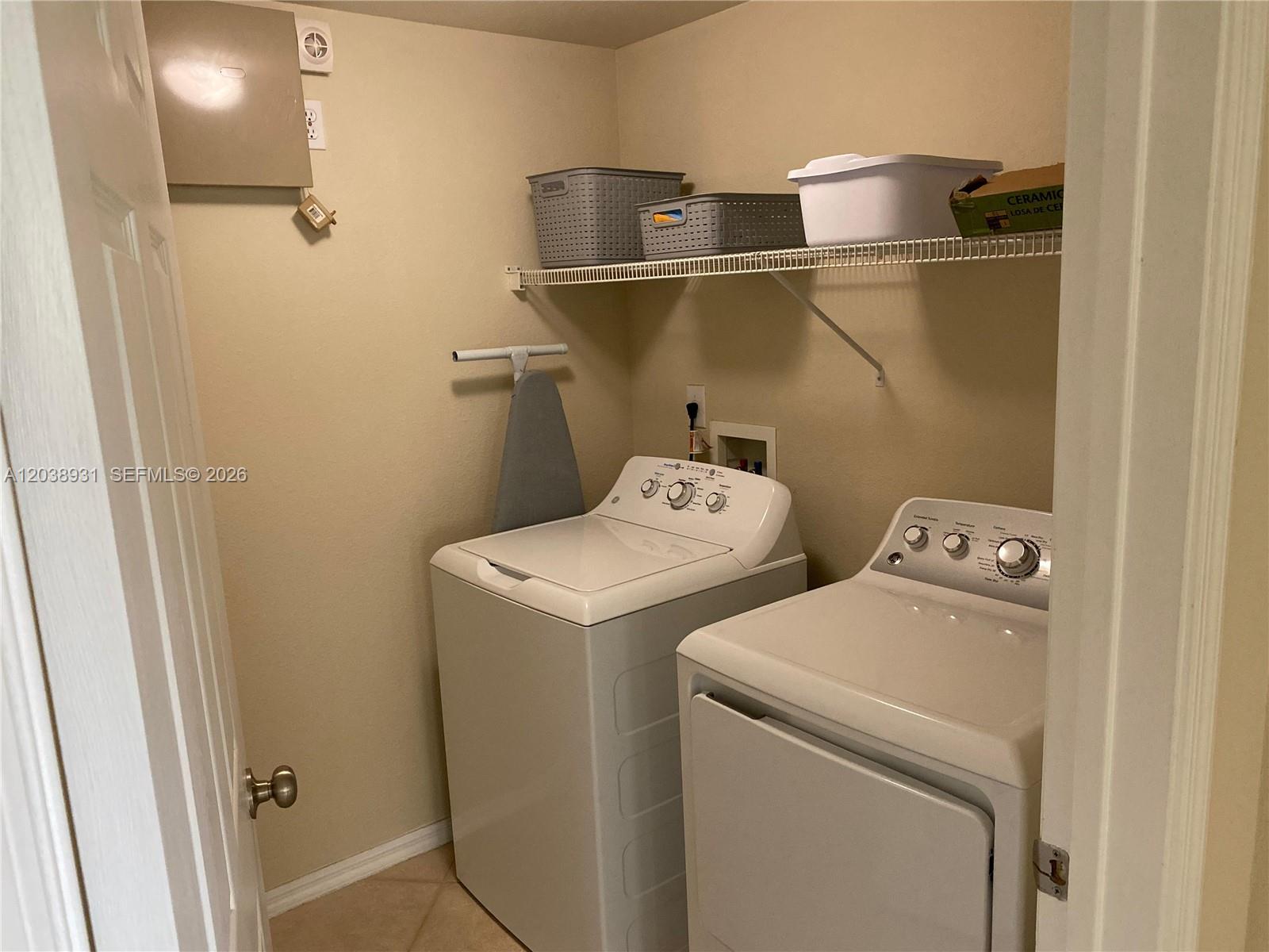 A laundry room features a white washer and dryer, a wire shelf, and an ironing board — 6400 Emerald Dunes Dr #303, West Palm Beach FL 33411, WEST PALM BEACH, FL