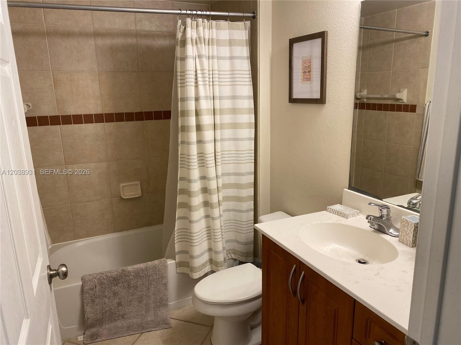This bathroom features a shower-tub combination, a vanity with a white countertop, and beige tiling — 6400 Emerald Dunes Dr #303, West Palm Beach FL 33411, WEST PALM BEACH, FL