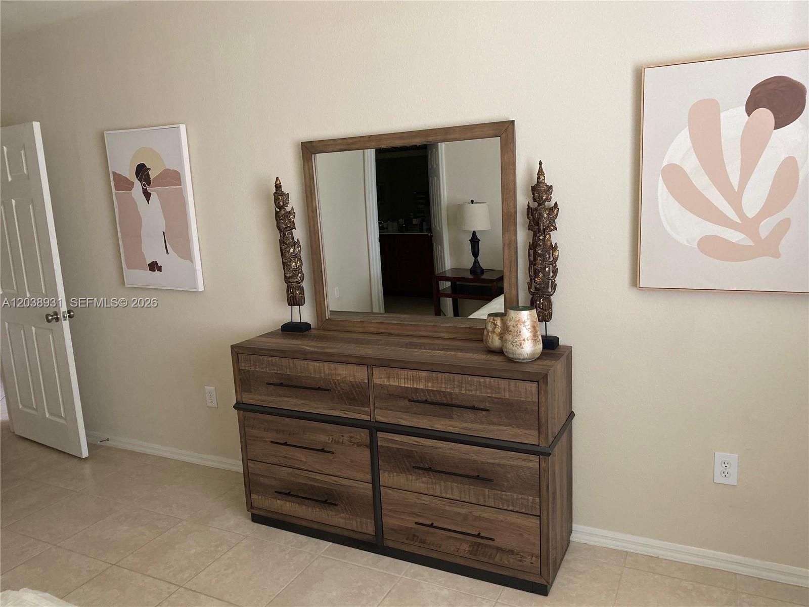 A wooden dresser with a mirror and two decorative statues sits against a beige wall — 6400 Emerald Dunes Dr #303, West Palm Beach FL 33411, WEST PALM BEACH, FL