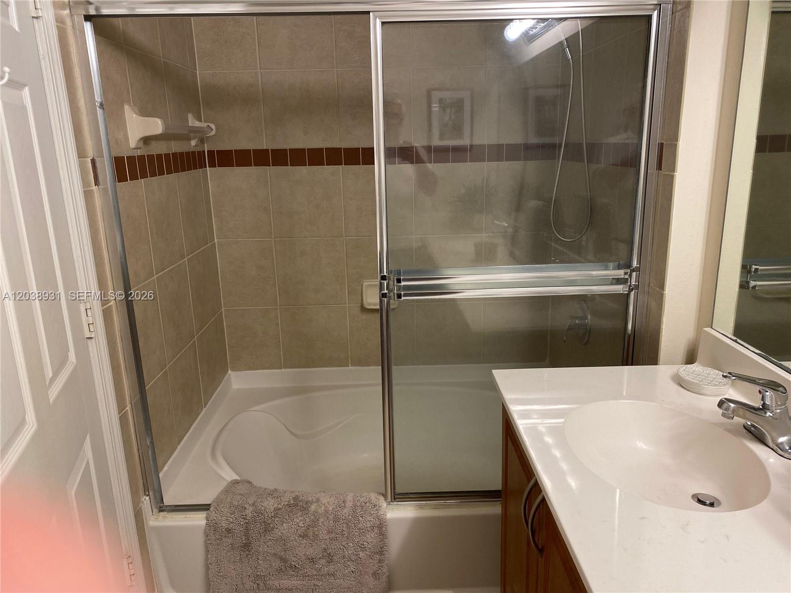 A bathroom features a tiled shower-tub combination with sliding glass doors and a vanity sink — 6400 Emerald Dunes Dr #303, West Palm Beach FL 33411, WEST PALM BEACH, FL