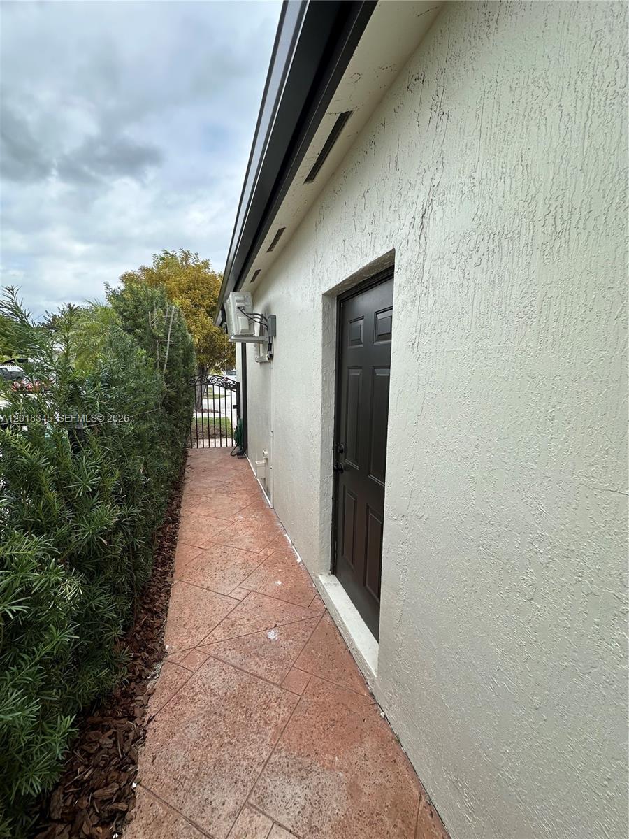 A narrow paved walkway runs alongside a stucco house wall with a dark door — MIAMI, FL