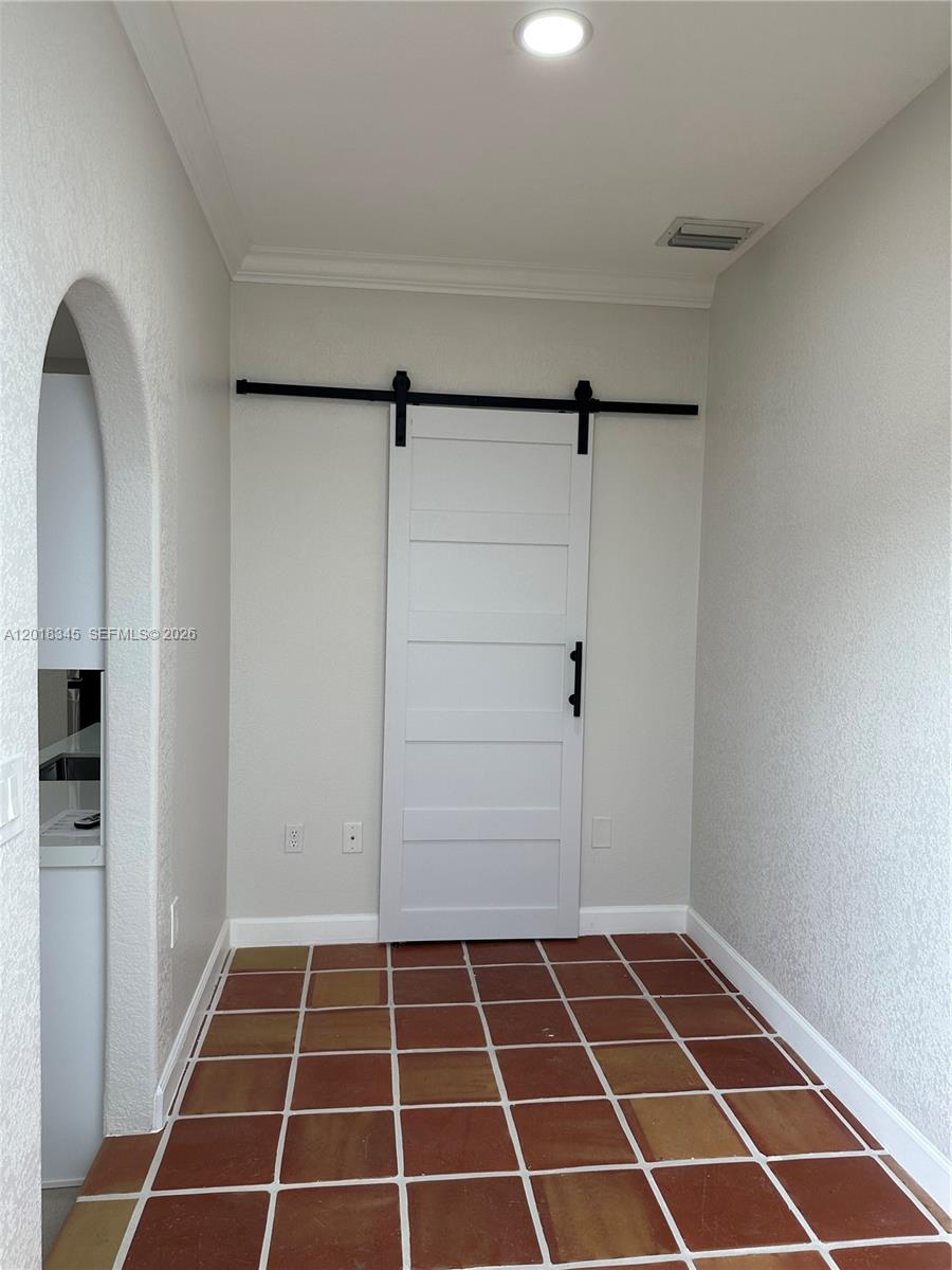 A hallway with terracotta tile flooring features a white sliding barn door on a track — MIAMI, FL