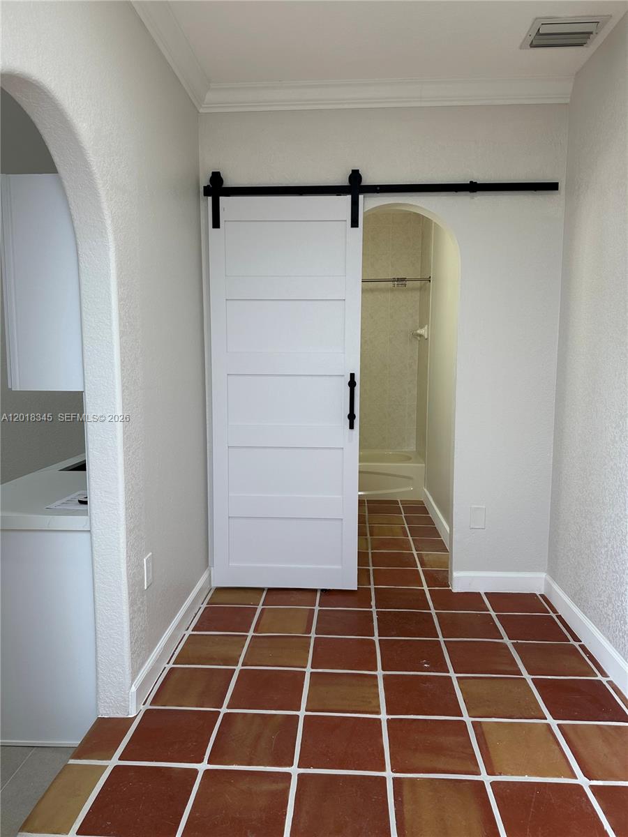 A white barn door opens to a bathroom with terracotta floor tiles and an archway — MIAMI, FL