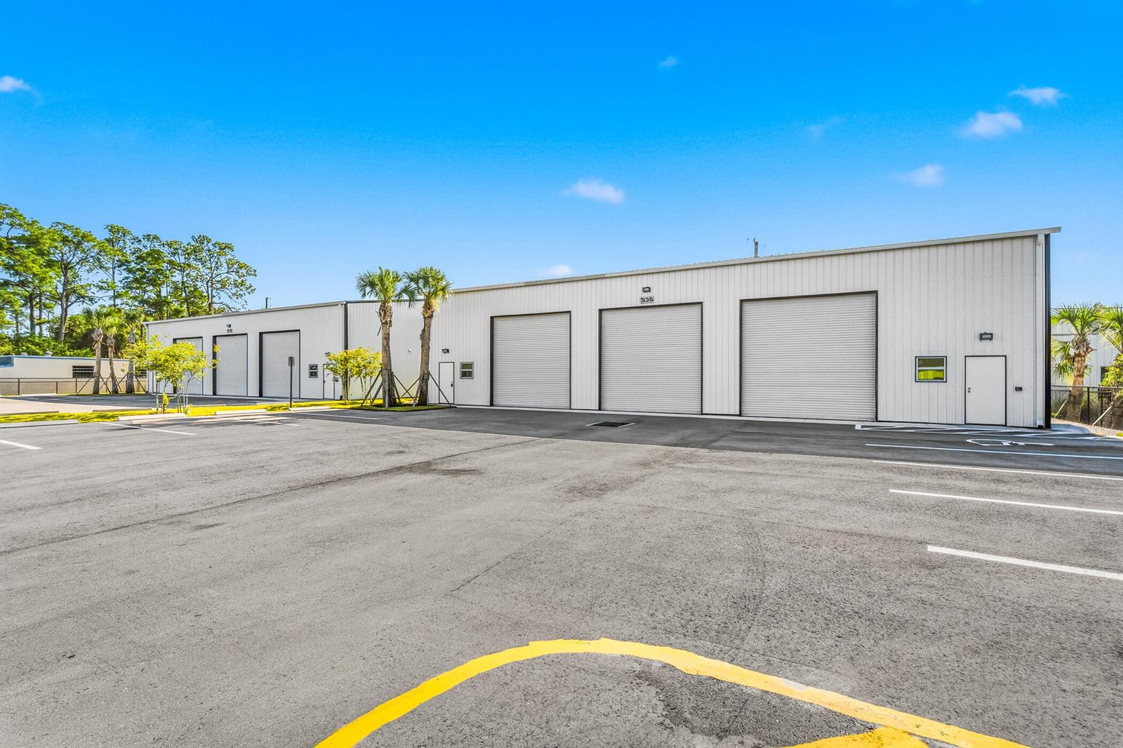 A long, white industrial warehouse building features multiple roll-up doors and a paved parking lot — VERO BEACH, FL