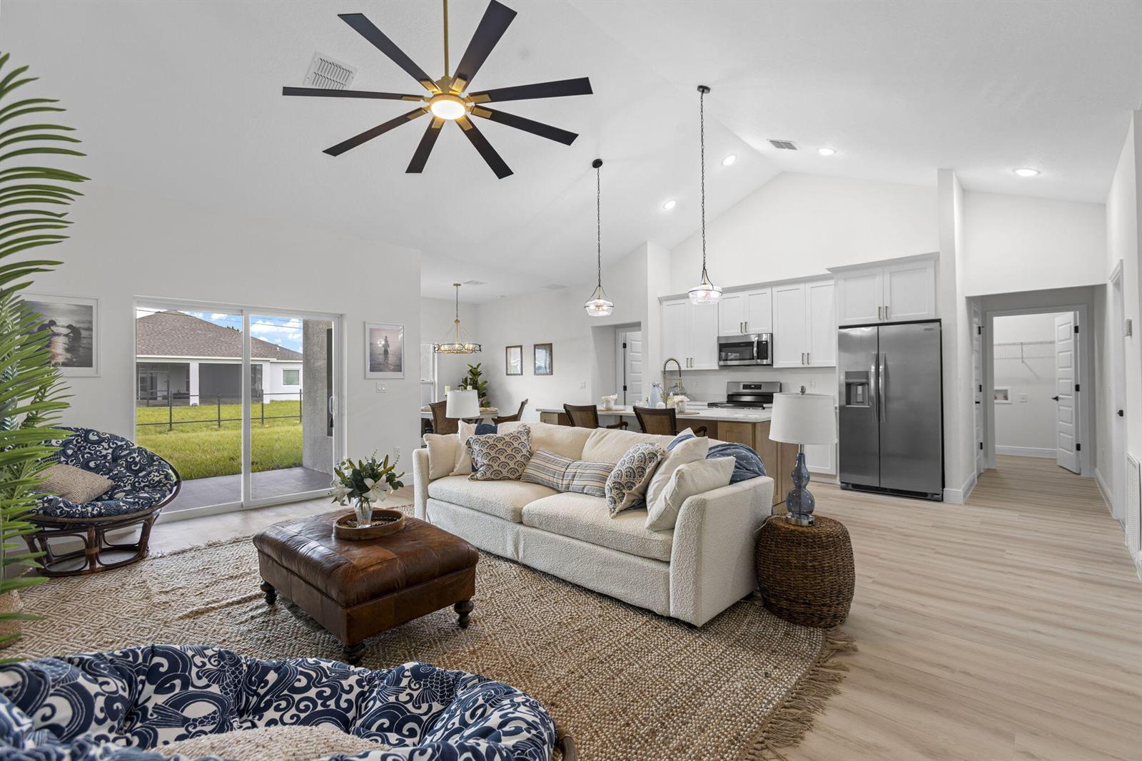 A bright, open-concept living room and kitchen featuring vaulted ceilings, white cabinetry, and wood flooring — 8536 96th Court, Vero Beach FL 32967, VERO BEACH, FL