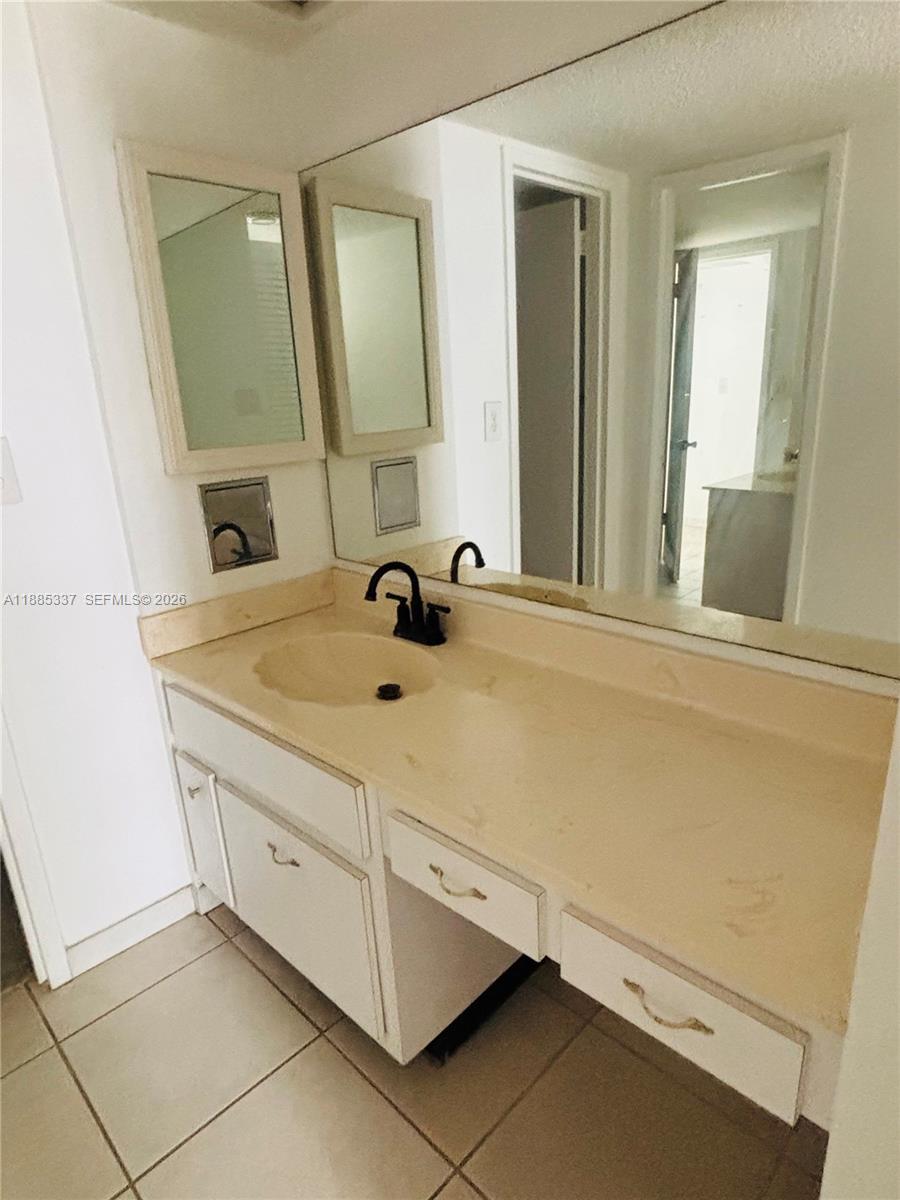 A bathroom features a vanity with a beige countertop, white cabinets, and a large mirror — 5701 Collins Ave # 709, Miami Beach FL 33140, MIAMI BEACH, FL