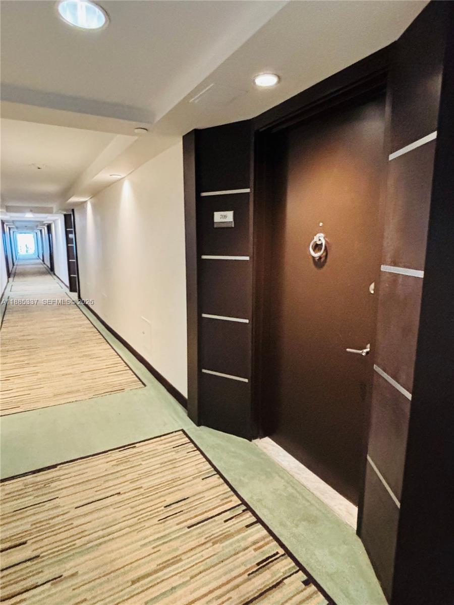 A long hallway with patterned carpet leads to a dark brown apartment door — 5701 Collins Ave # 709, Miami Beach FL 33140, MIAMI BEACH, FL