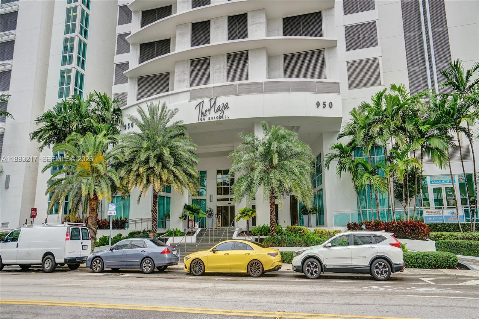 The exterior of a white high-rise building with palm trees and parked cars in front — 950 Brickell Bay Dr # 1704, Miami FL 33131, MIAMI, FL