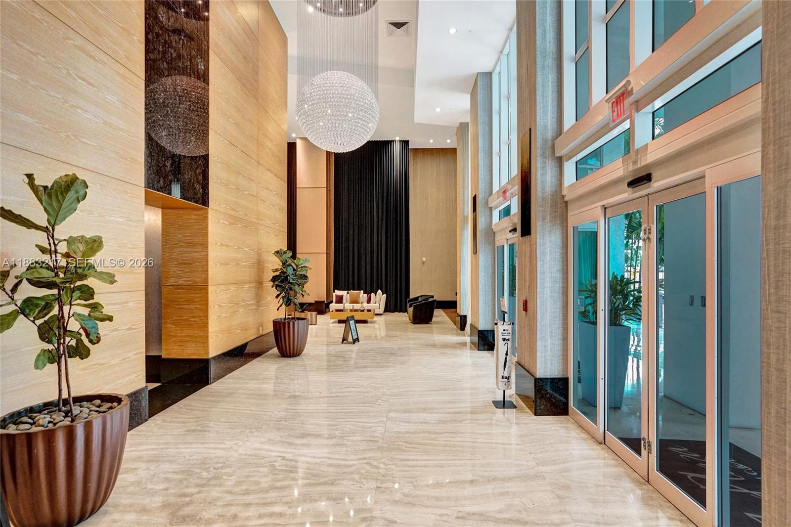 A modern lobby features a large crystal chandelier, wood-paneled walls, and polished stone flooring — 950 Brickell Bay Dr # 1704, Miami FL 33131, MIAMI, FL