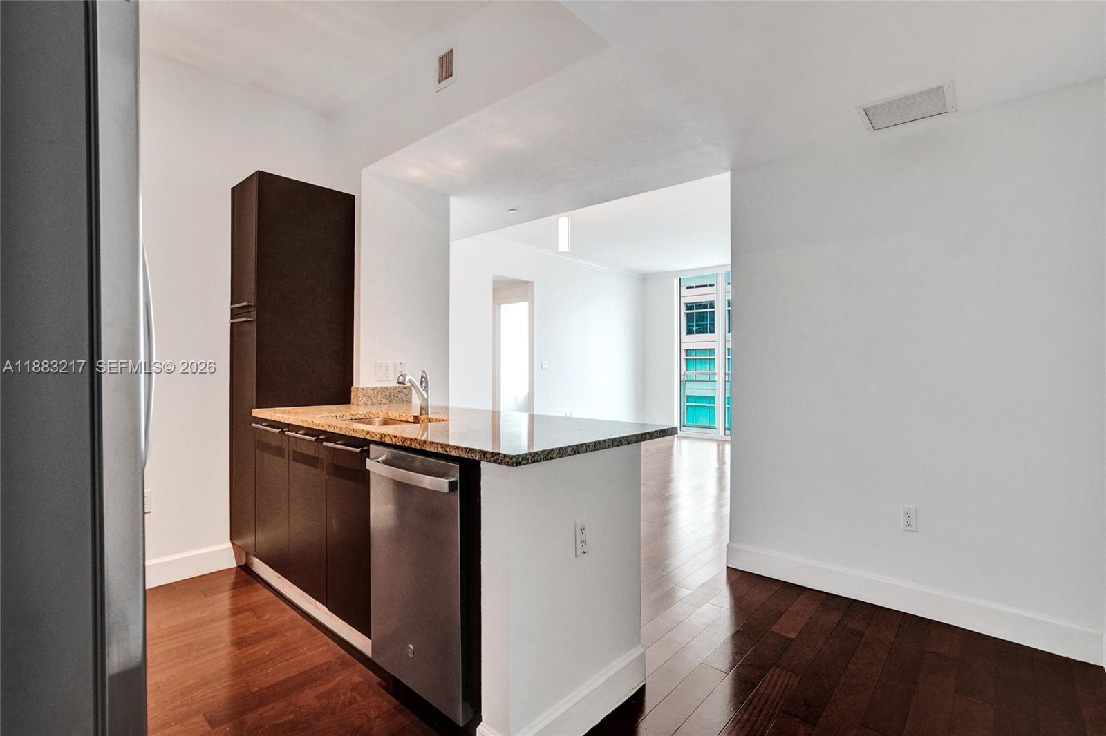 A kitchen with dark cabinets and granite countertops overlooks an open living area — 950 Brickell Bay Dr # 1704, Miami FL 33131, MIAMI, FL