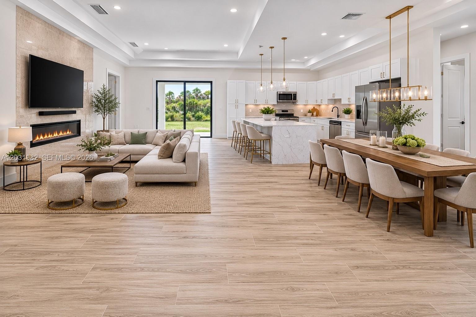 An open-concept living area features a modern kitchen, dining space, and fireplace with wood-look tile — 2622 22 Avenue SE, Naples FL 34117, NAPLES, FL