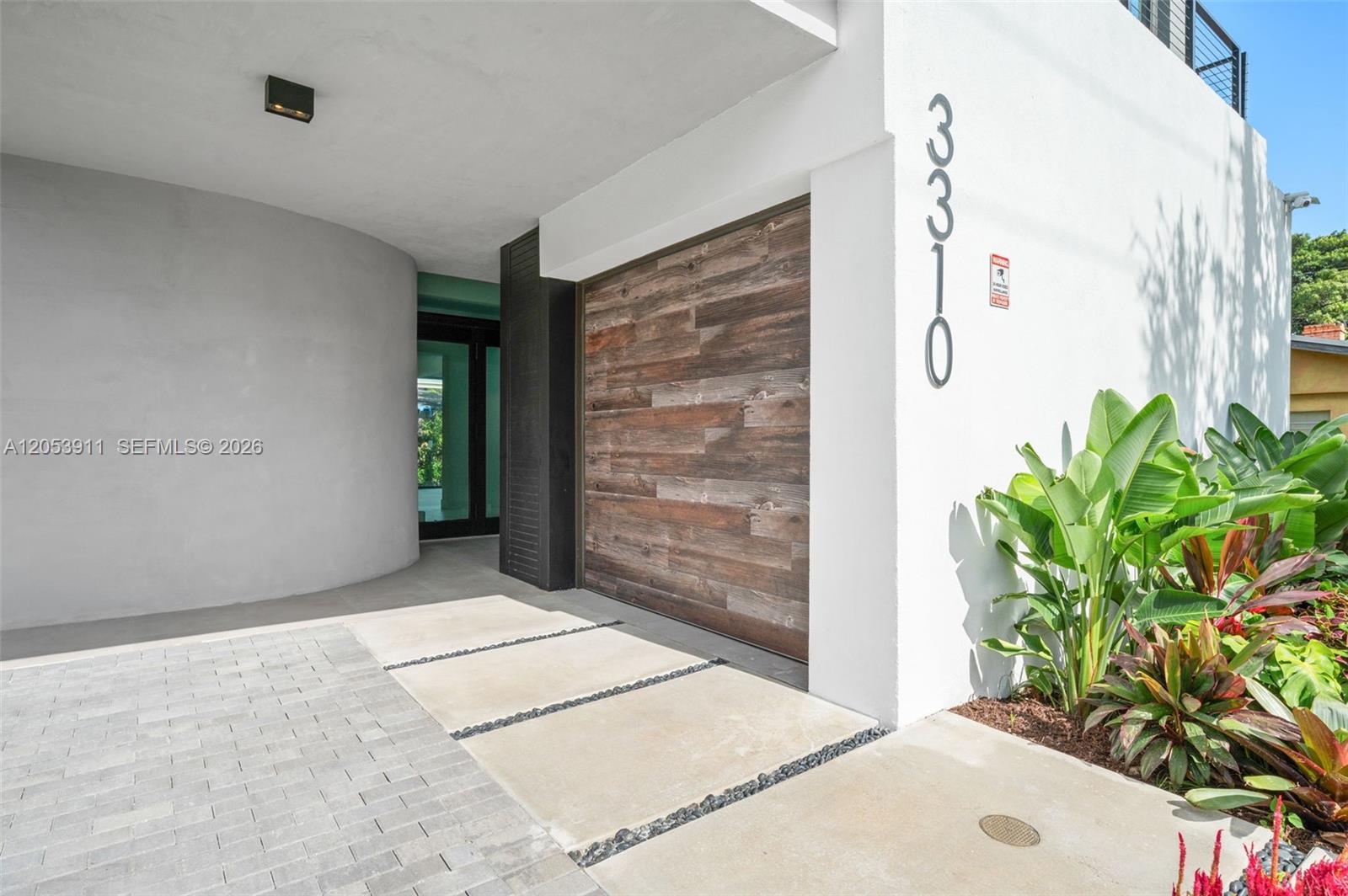 A modern home exterior features a wood-paneled garage door, white walls, and a paved driveway — 3310 Elizabeth St, Miami FL 33133, MIAMI, FL
